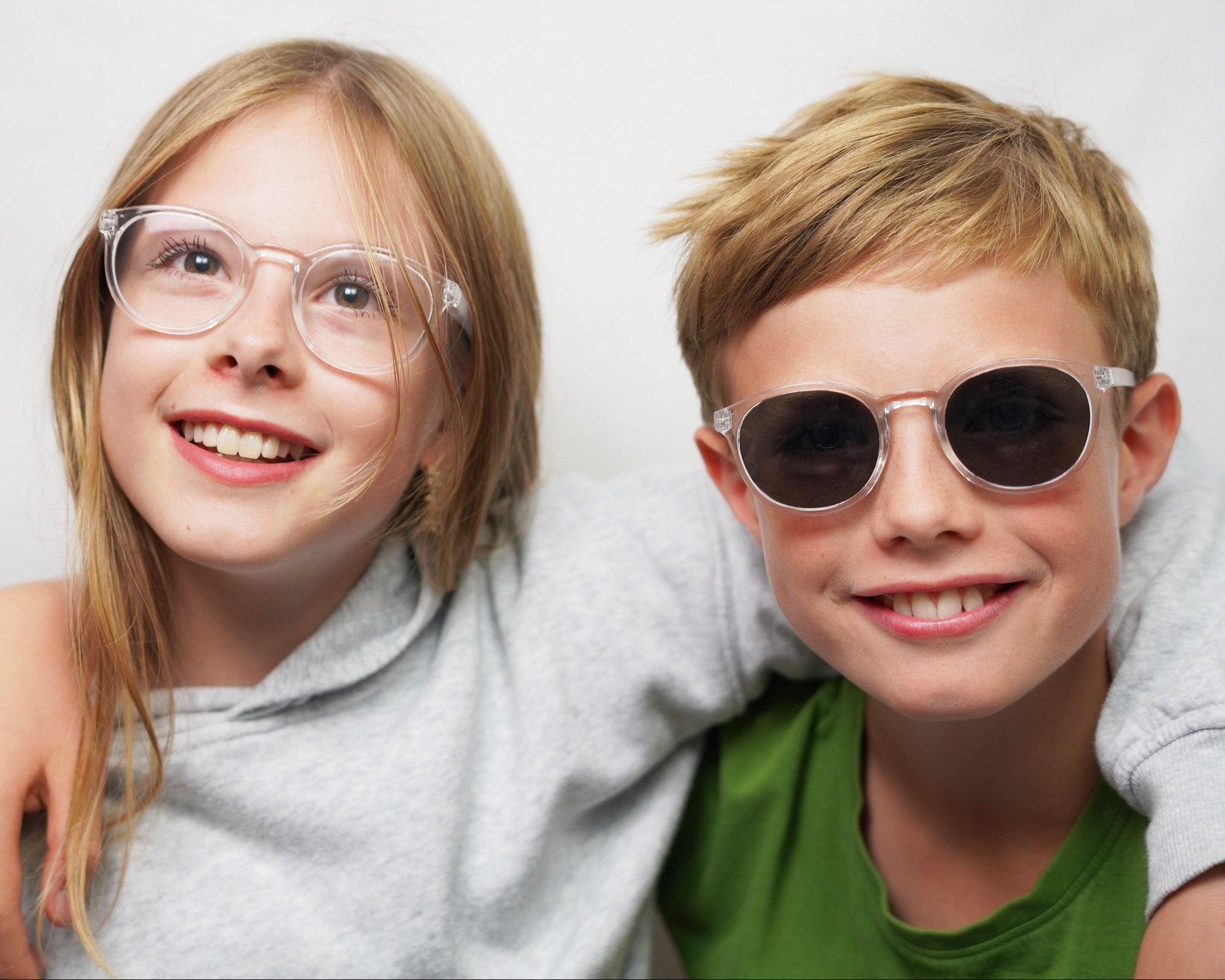 Two teenager wearing Klammeraffe sunglasses and blue light glasses and smiling against a white background.
