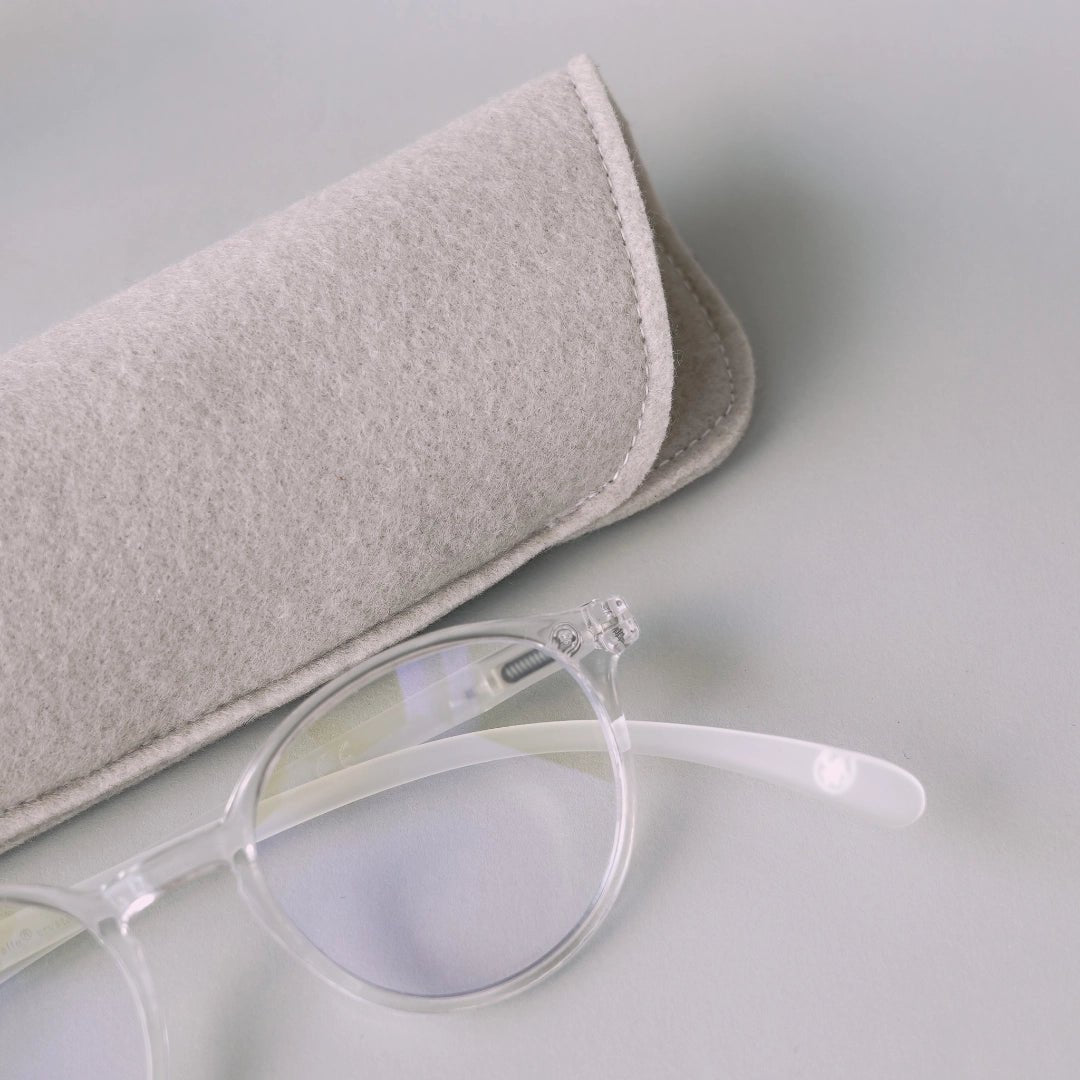 Klammeraffe No.12 blue light glasses in crystal color with longer temples together with the case on a gray underground.