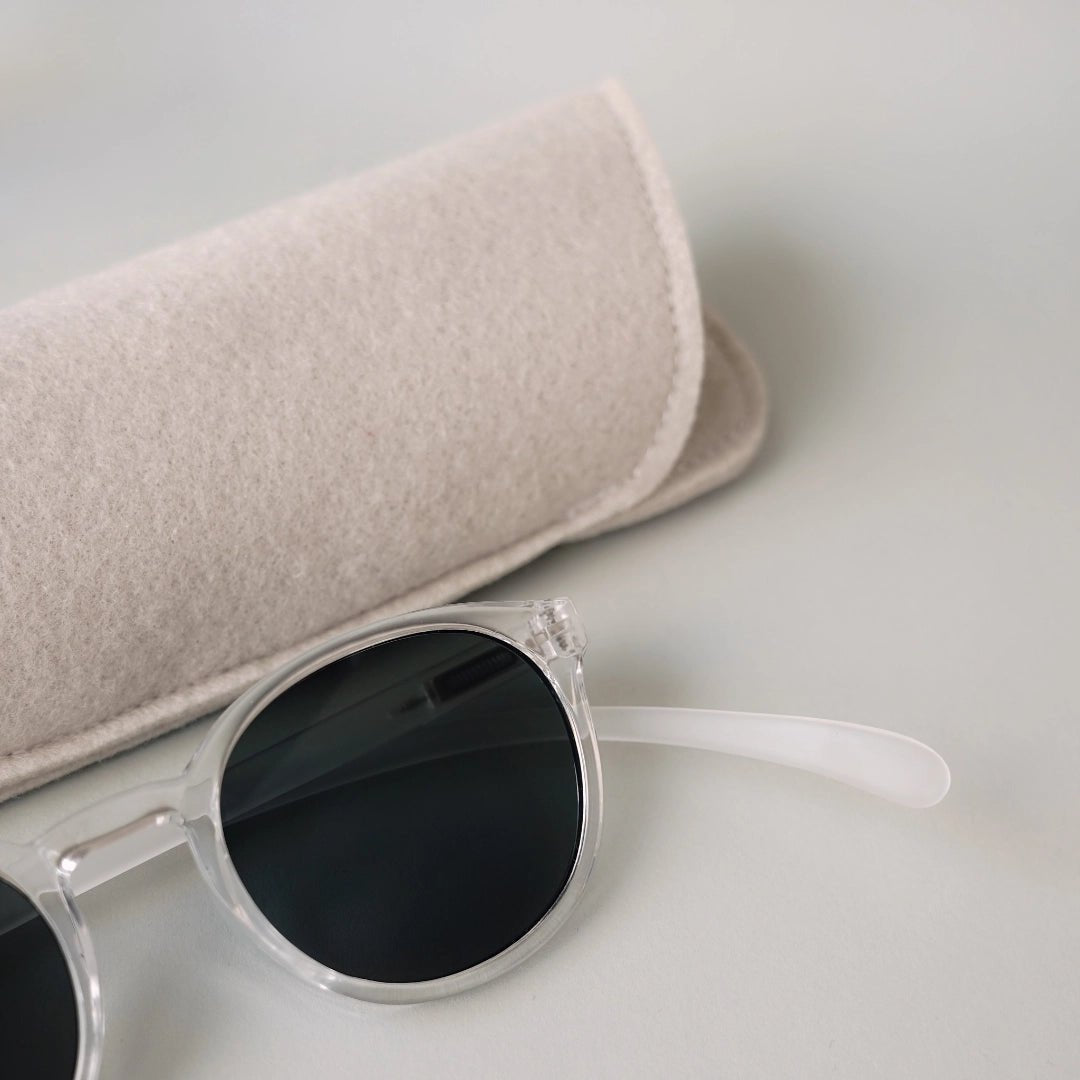 Klammeraffe No.13 sunglasses in crystal color with longer temples together with the case on a gray underground.